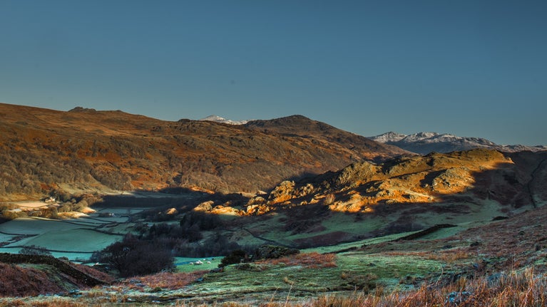 View into Duddon Valley on a clear winter's day with bracken in the foreground and snow dusted fells in the distance.